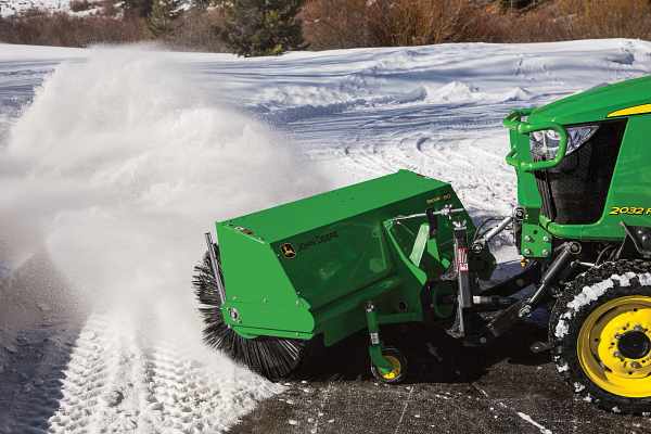 Side left view of the front of a 2032R compact tractor with front-attached 60-in. Heavy-Duty Rotary Broom blowing snow from pavement