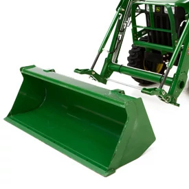 Studio front left image of a loader resting on the floor, ready to be attached to the quick-change attachment carrier on the tractor behind it