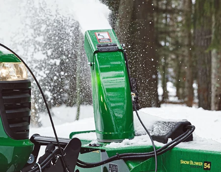 Close-up of a snow blower showing the discharge chute throwing snow upward.