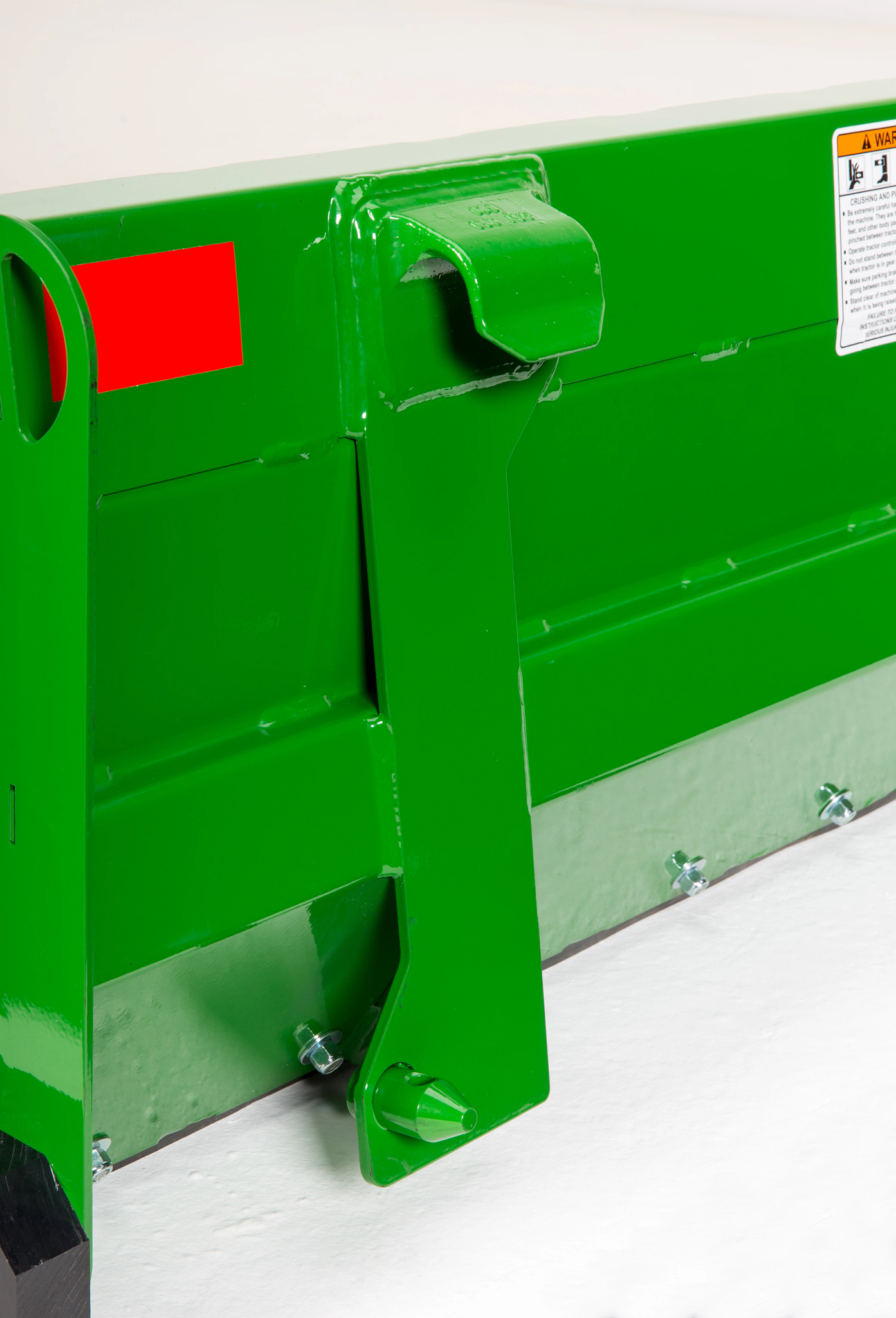 Close-up of steel blade showing a reinforced end plate with welded seams, a mounting hook, reflective red decal, and a bolted metal wear edge along the bottom.