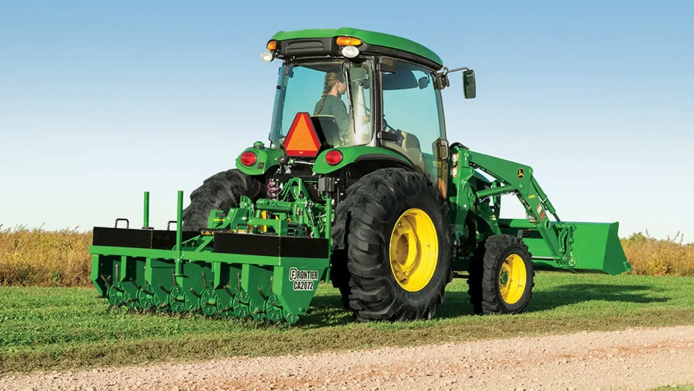 Tractor with a CA2072 Core Aerator aerating grass along a small gravel road