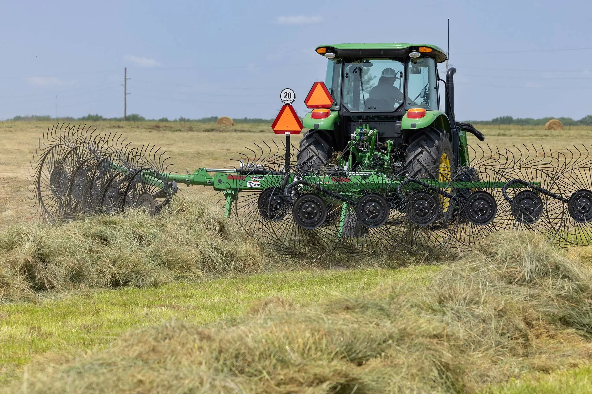 Rear view of a 5100E tractor working a hay field with a WR3212 wheel rake