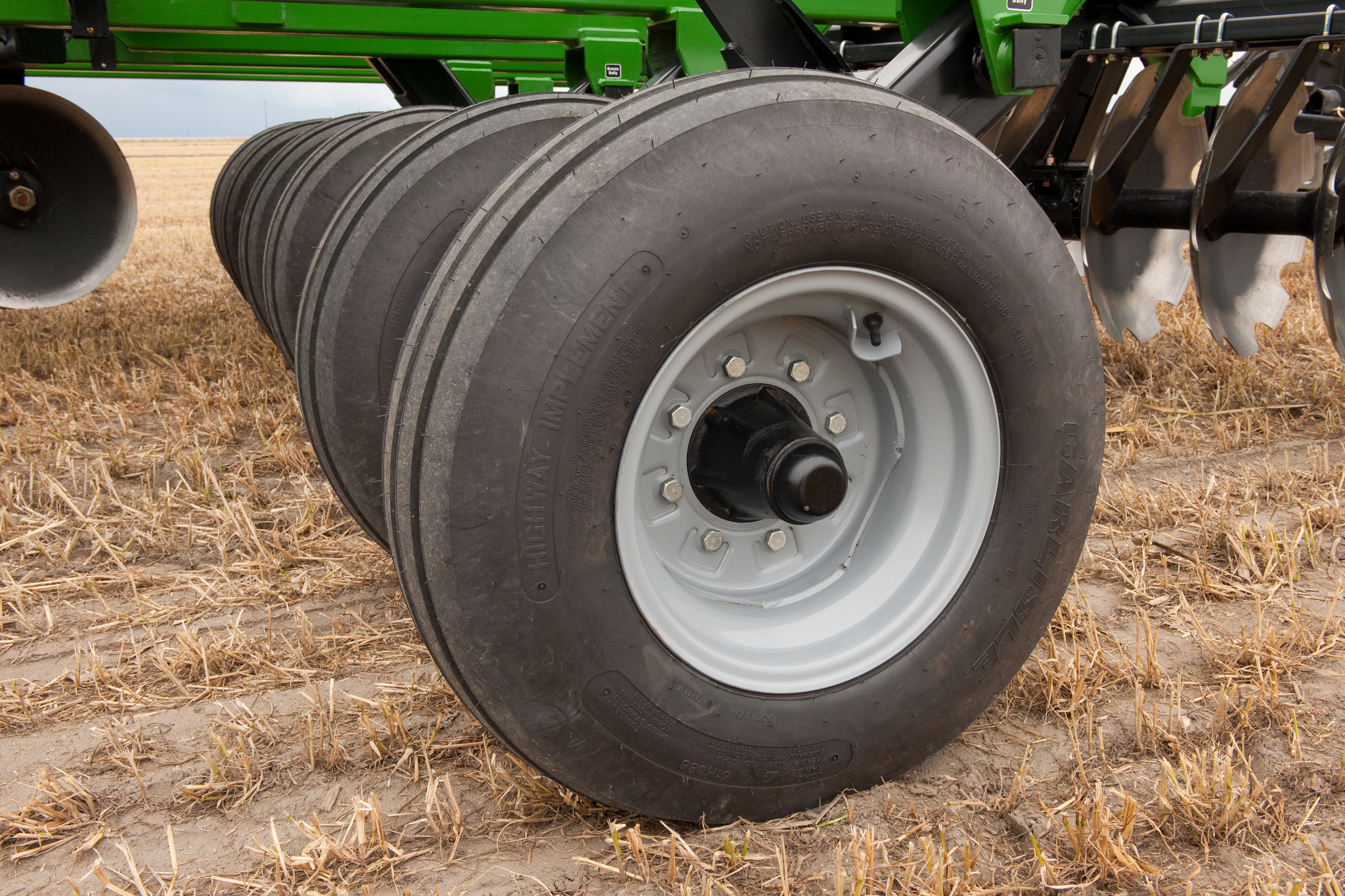 Close-up side view of the TM51 series tandem disk harrow's line of dual wheels resting on a golden field