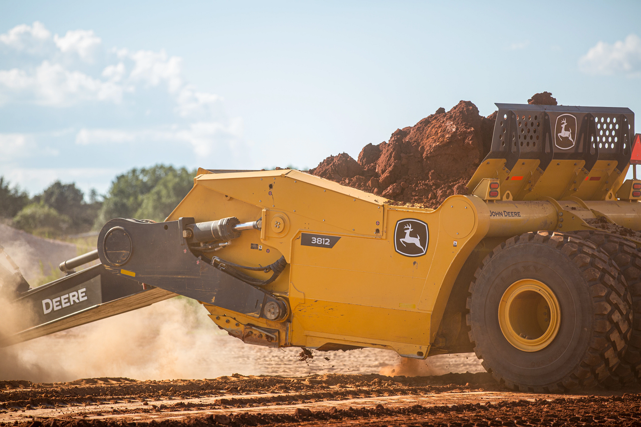 Side left view of a 3812 Scraper loaded with dirt at a sunny jobsite