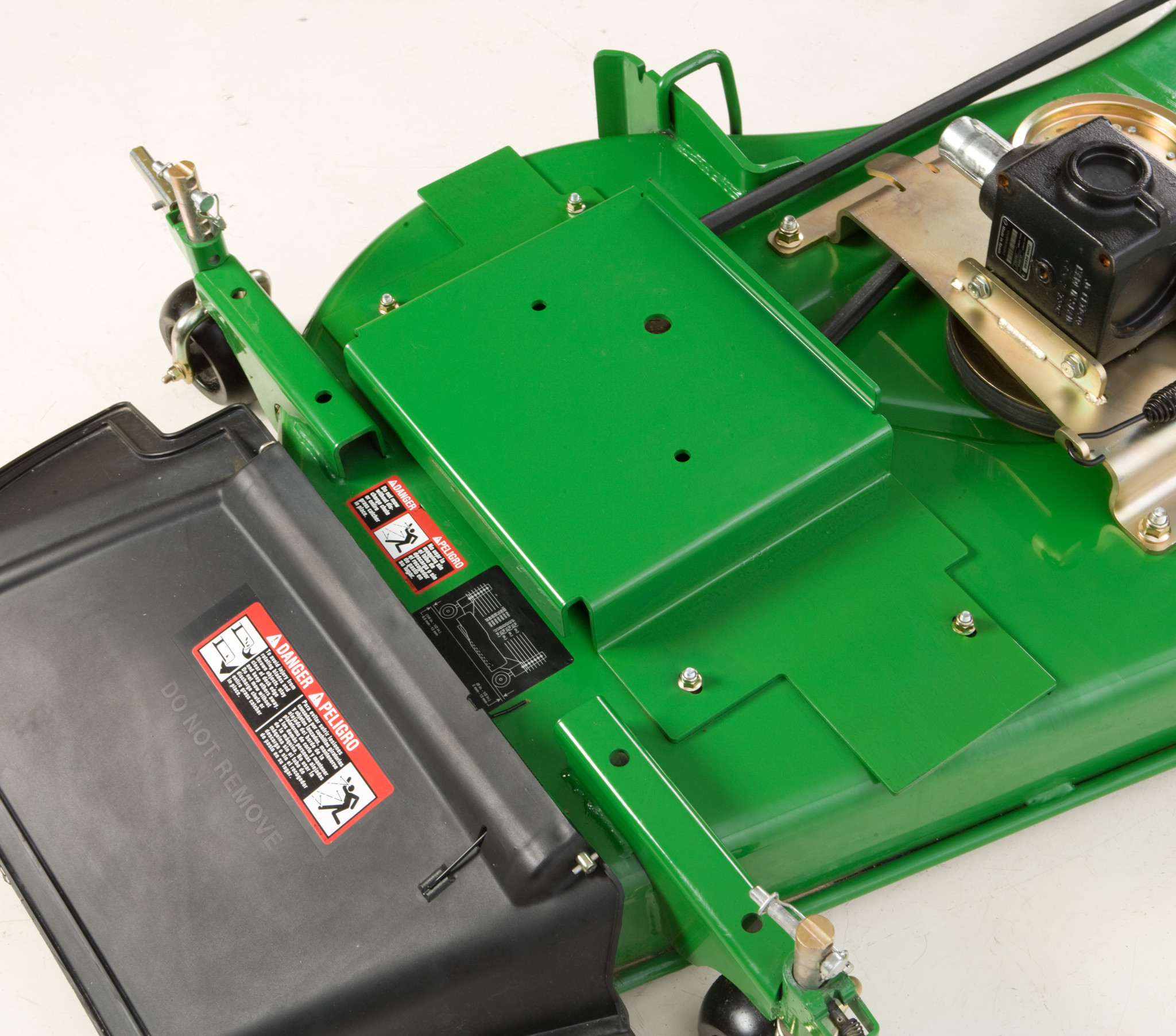 Close-up top view of a green mower deck showing the discharge chute, warning labels, belt cover, and pulley assembly