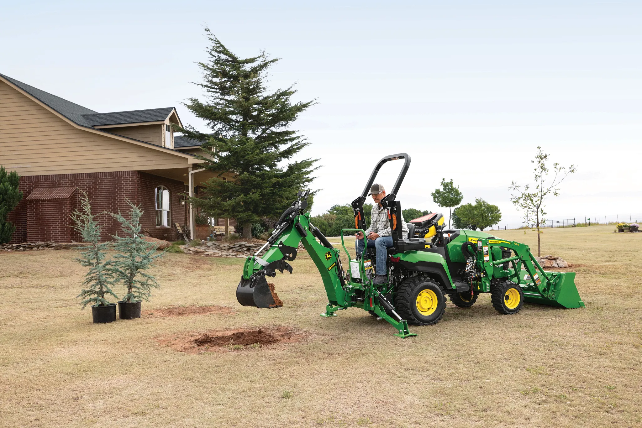 A green tractor with a front loader and backhoe a open yard