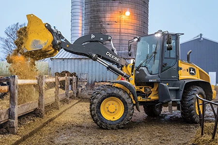 Side left view of a 344 P-Tier Compact Wheel Loader dumping material over a fence at a farm