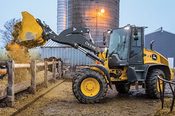 Side left view of a 344 P-Tier Compact Wheel Loader dumping material over a fence at a farm