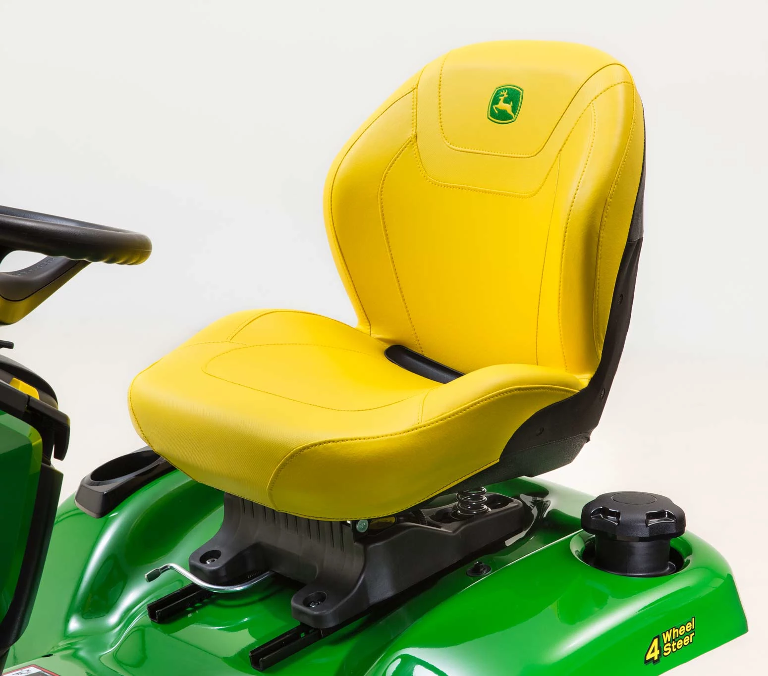 Front left studio view of an X394 lawn tractor's yellow operator seat and "4 wheel steer" decal on the green fender beside it