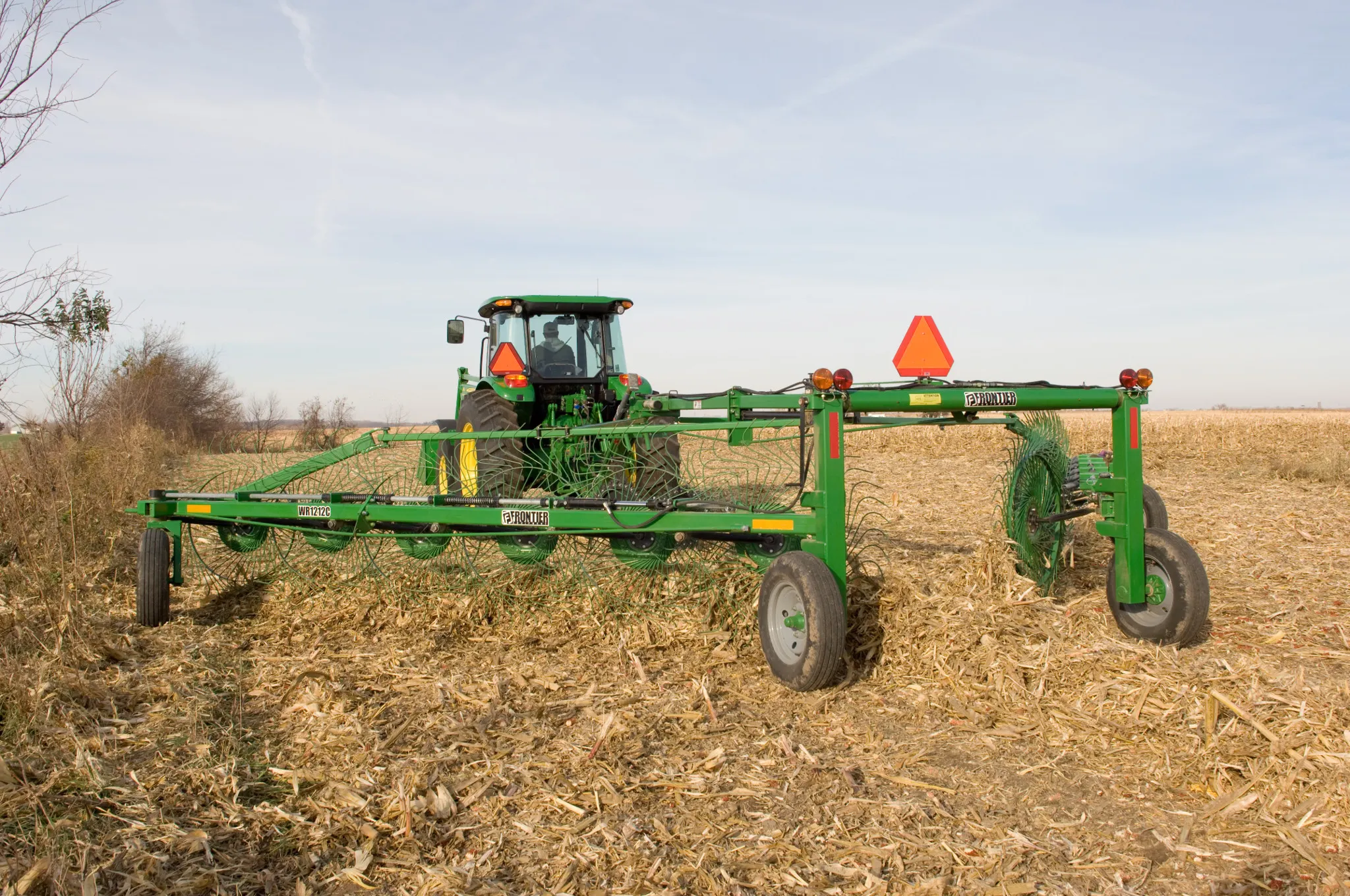 Rear view of a WR1212 High-Capacity Wheel Rake being pulled across a harvested field by a tractor