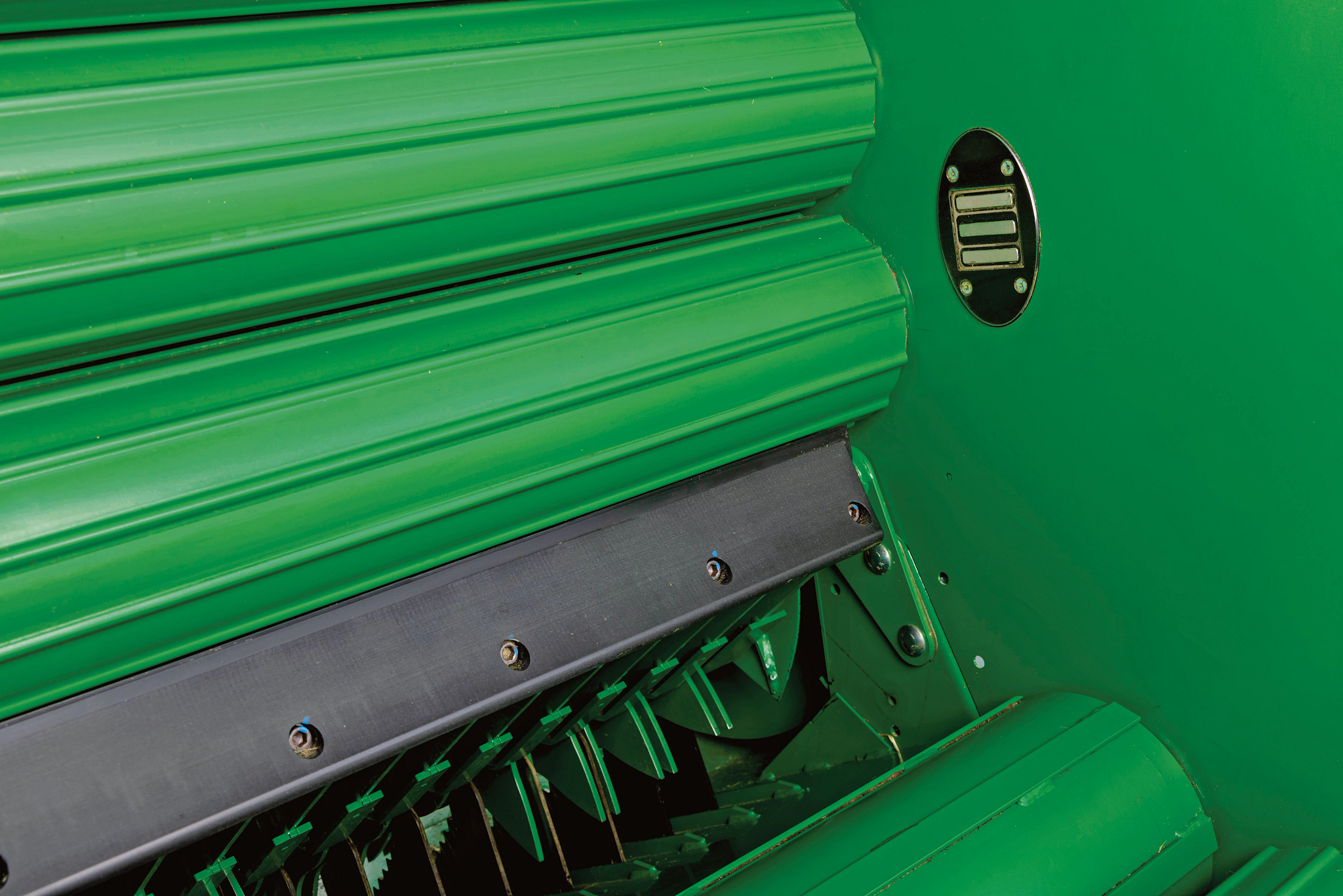 Close-up view inside a John Deere baler showing green feed rollers and cutting components in the baling chamber, with hay material moving through the mechanism.