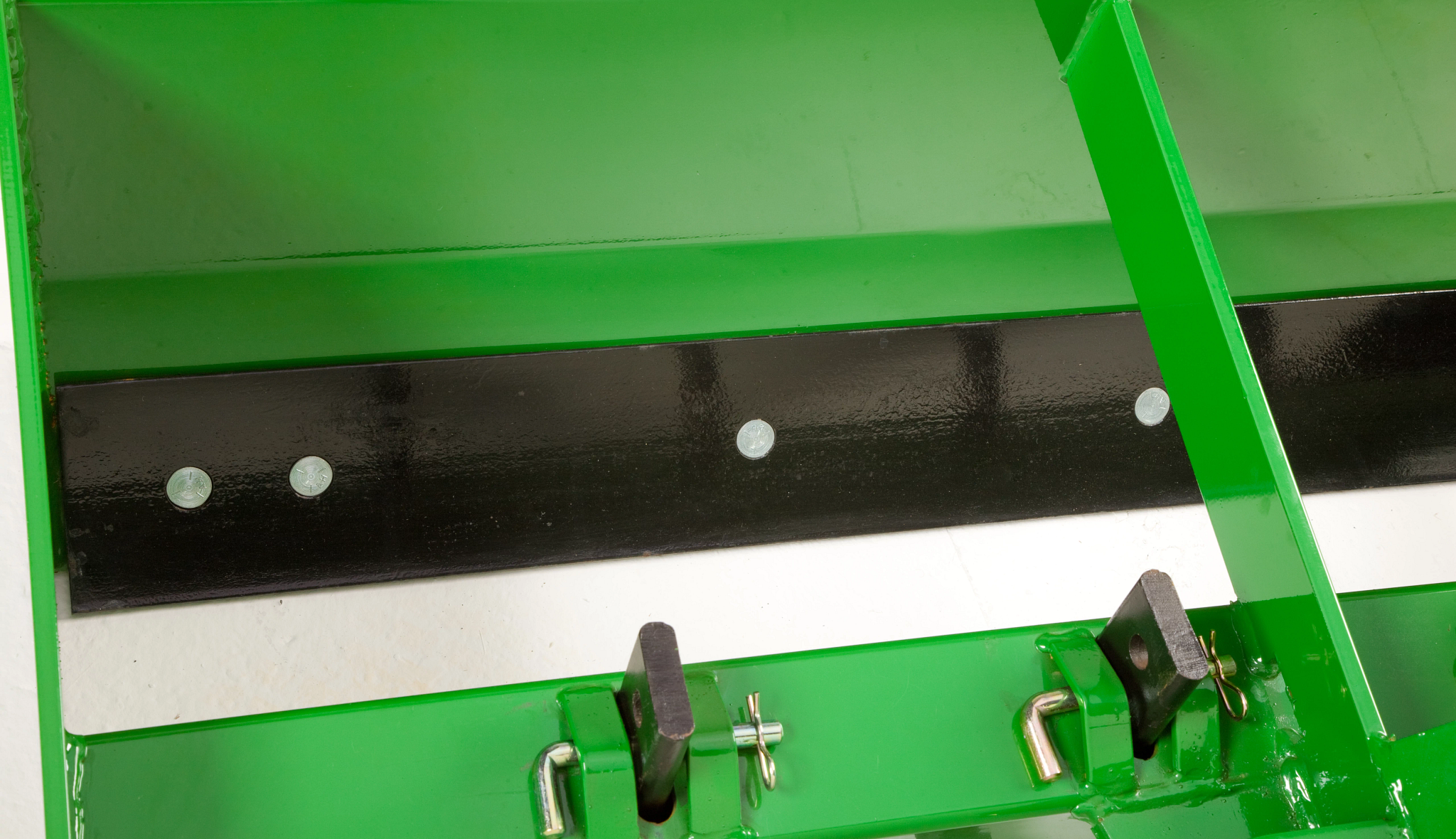 Close-up of agricultural implement showing adjustable mounting brackets with locking pins and clips beneath a black wear strip.