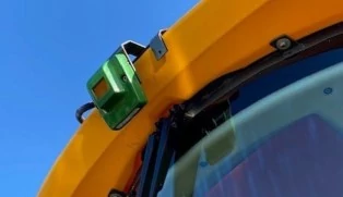 Close‑up of a green camera system attached to the yellow roof of a self-propelled sprayer against a blue sky