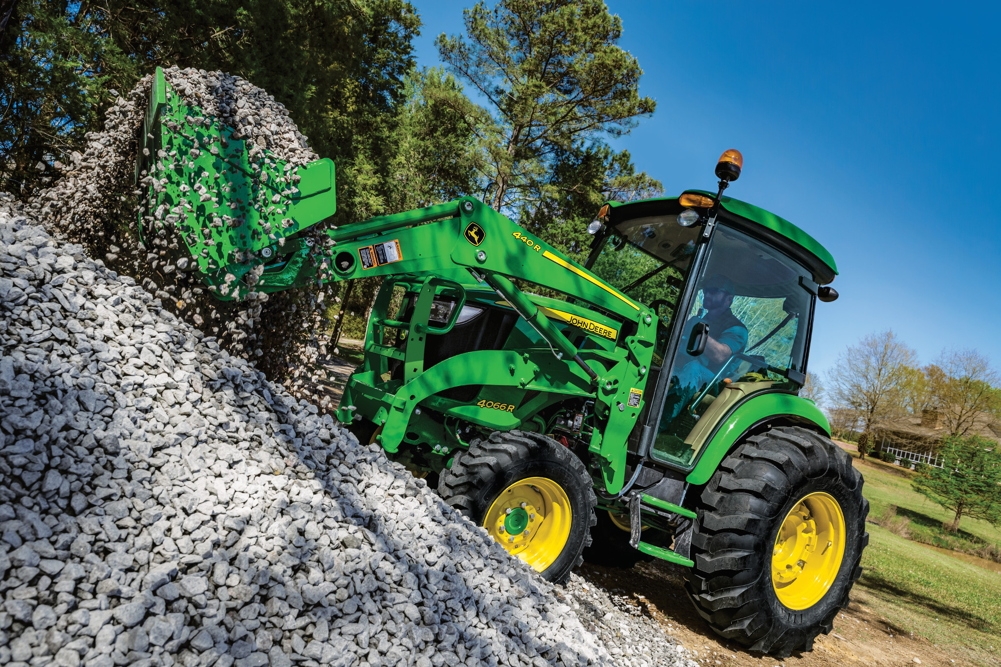 John Deere 4066R cab tractor using its loader and bucket to move gravel