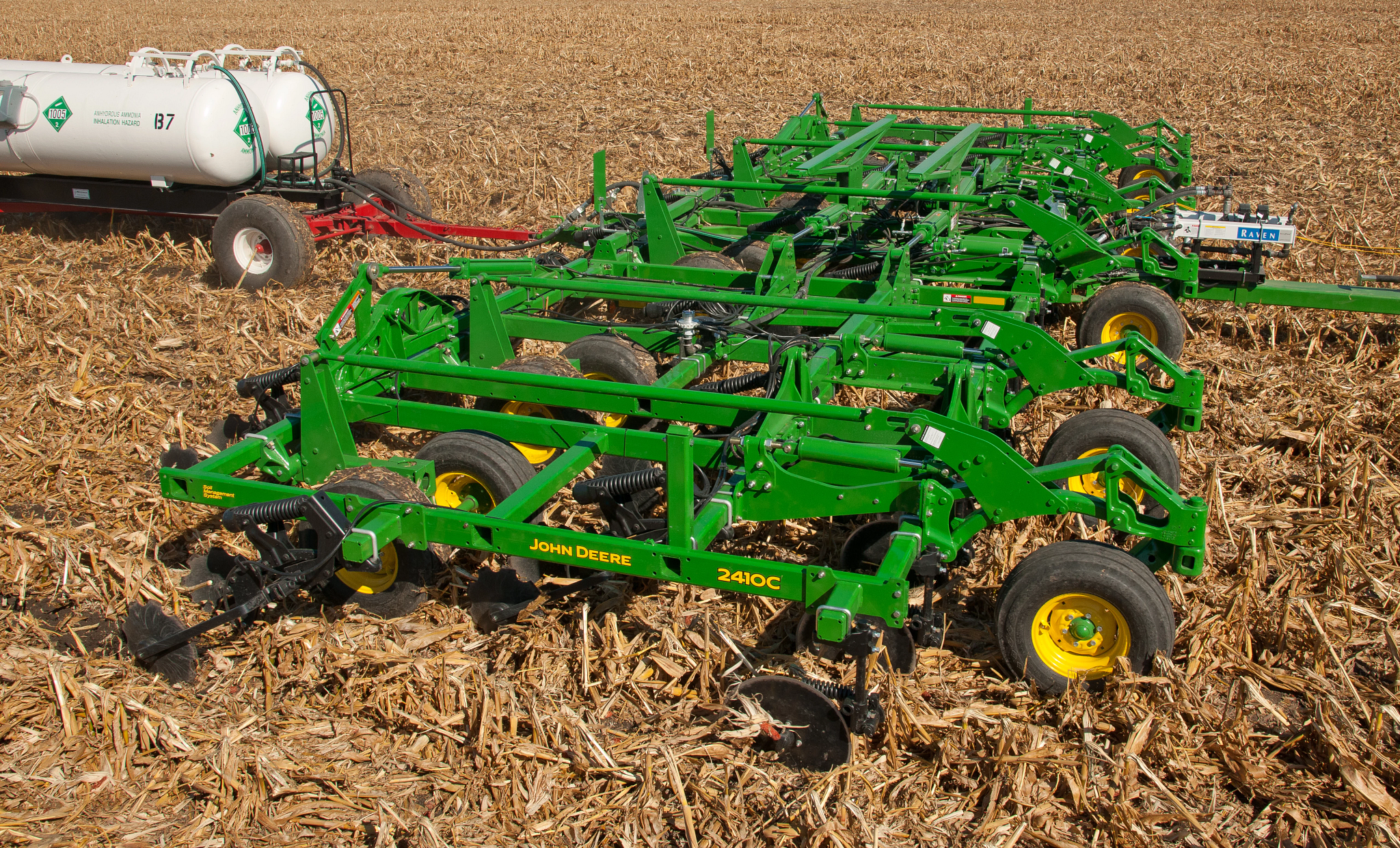 Green nutrient applicator in a harvested field, showing the frame, wheels, and ground‑engaging components with an attached anhydrous ammonia tank