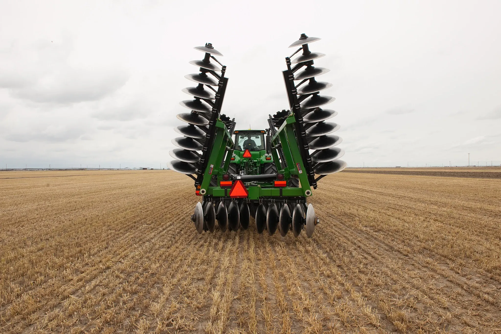 Distant rear view of a tractor pulling a Frontier Tandem 51 Series Disk Harrow in the field