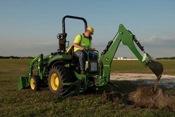 Front angled view of an operator on an open station tractor using an attached 270B backhoe in a field