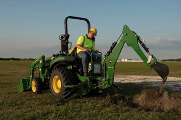 Front angled view of an operator on an open station tractor using an attached 270B backhoe in a field