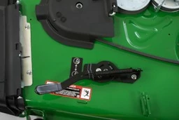 Close-up of a John Deere mower deck showing the black height‑adjustment lever with return spring, adjustment icon, and warning label mounted on the green deck surface.