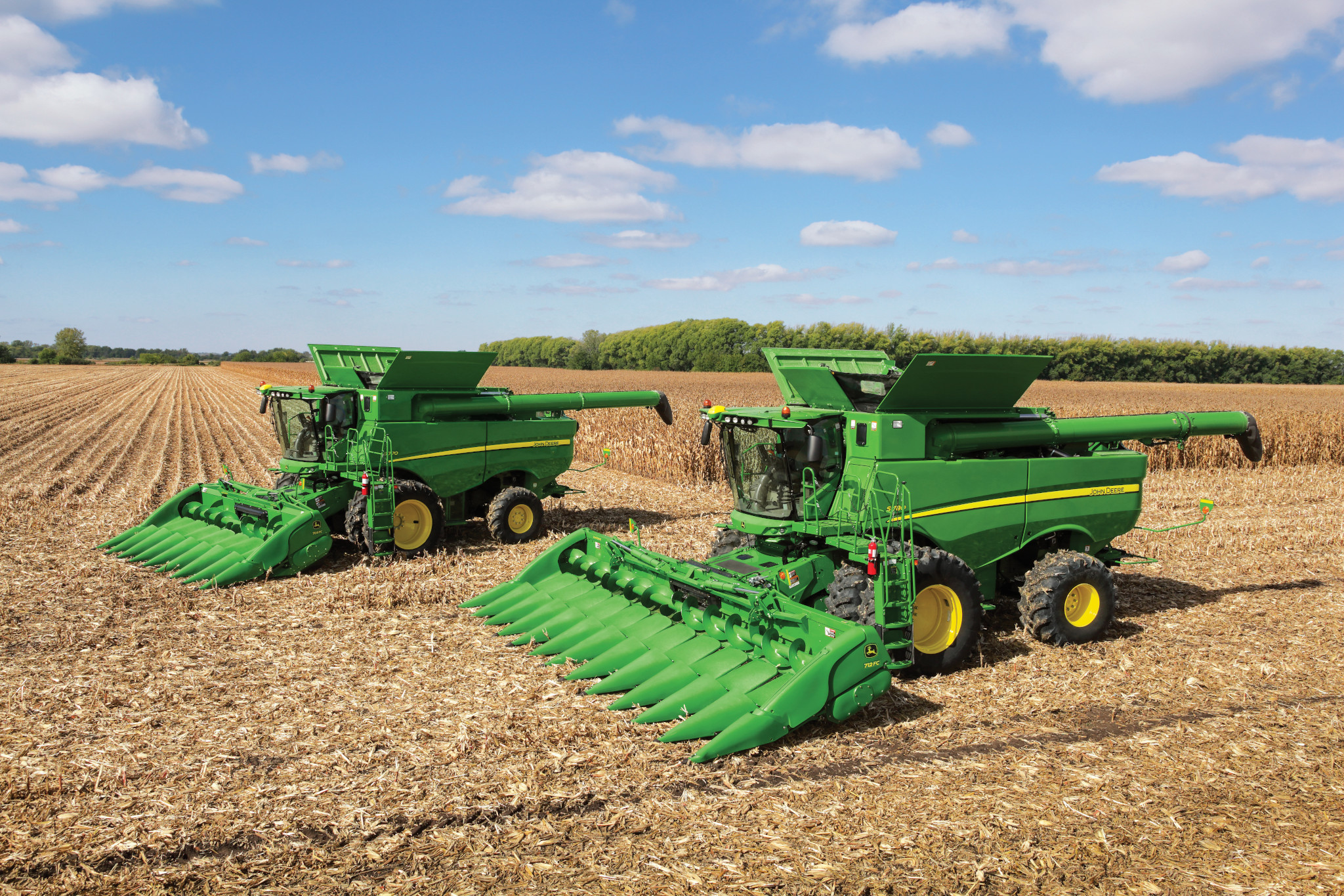 John Deere combines with corn heads in a harvested field