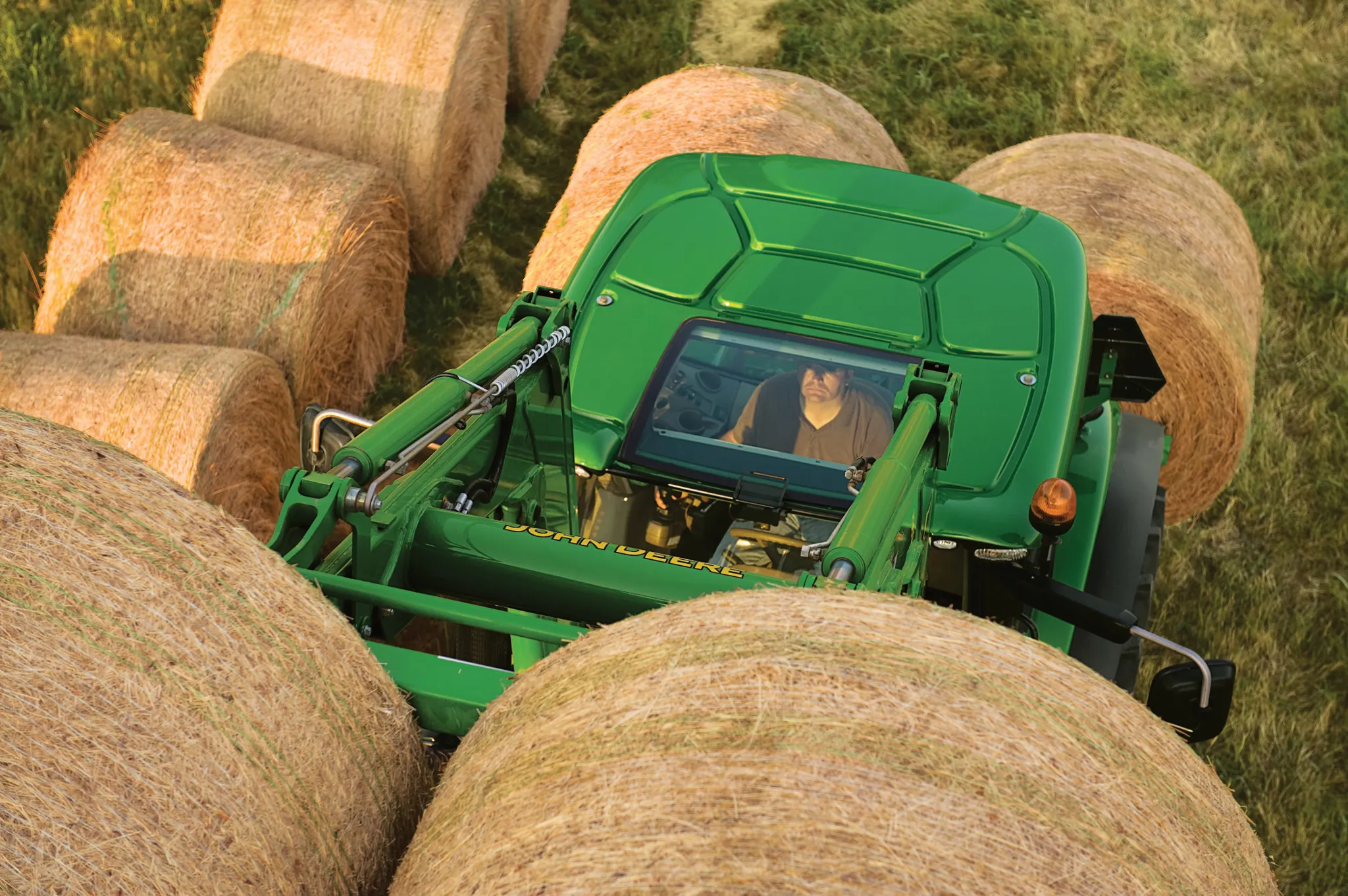 A tractor with a bale spear attachment surrounded by large, round hay bales in a field