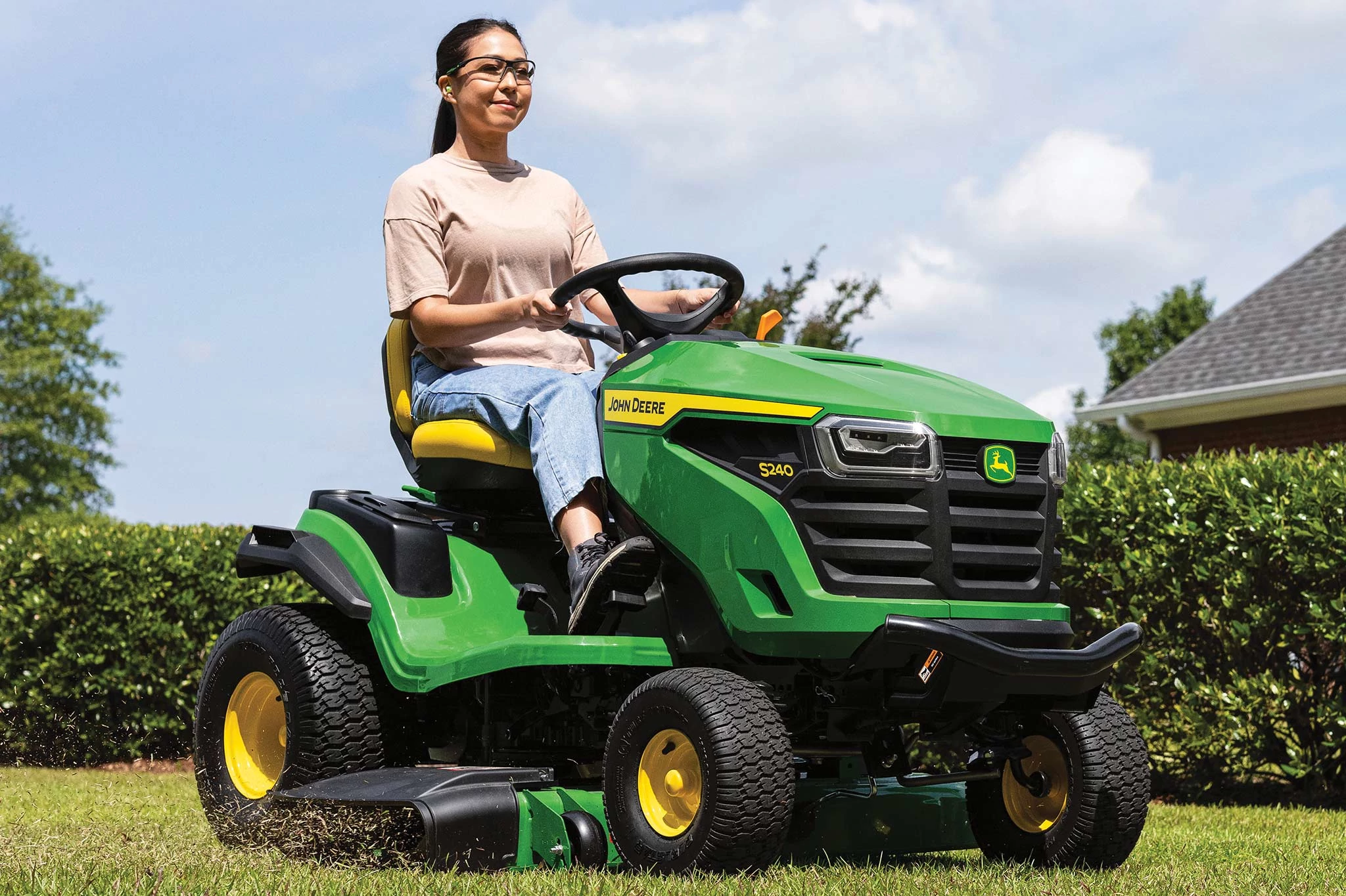 Front right view of a homeowner driving an S240 Lawn Tractor with 42-in. Accel Deep mower deck on a hedge-lined lawn