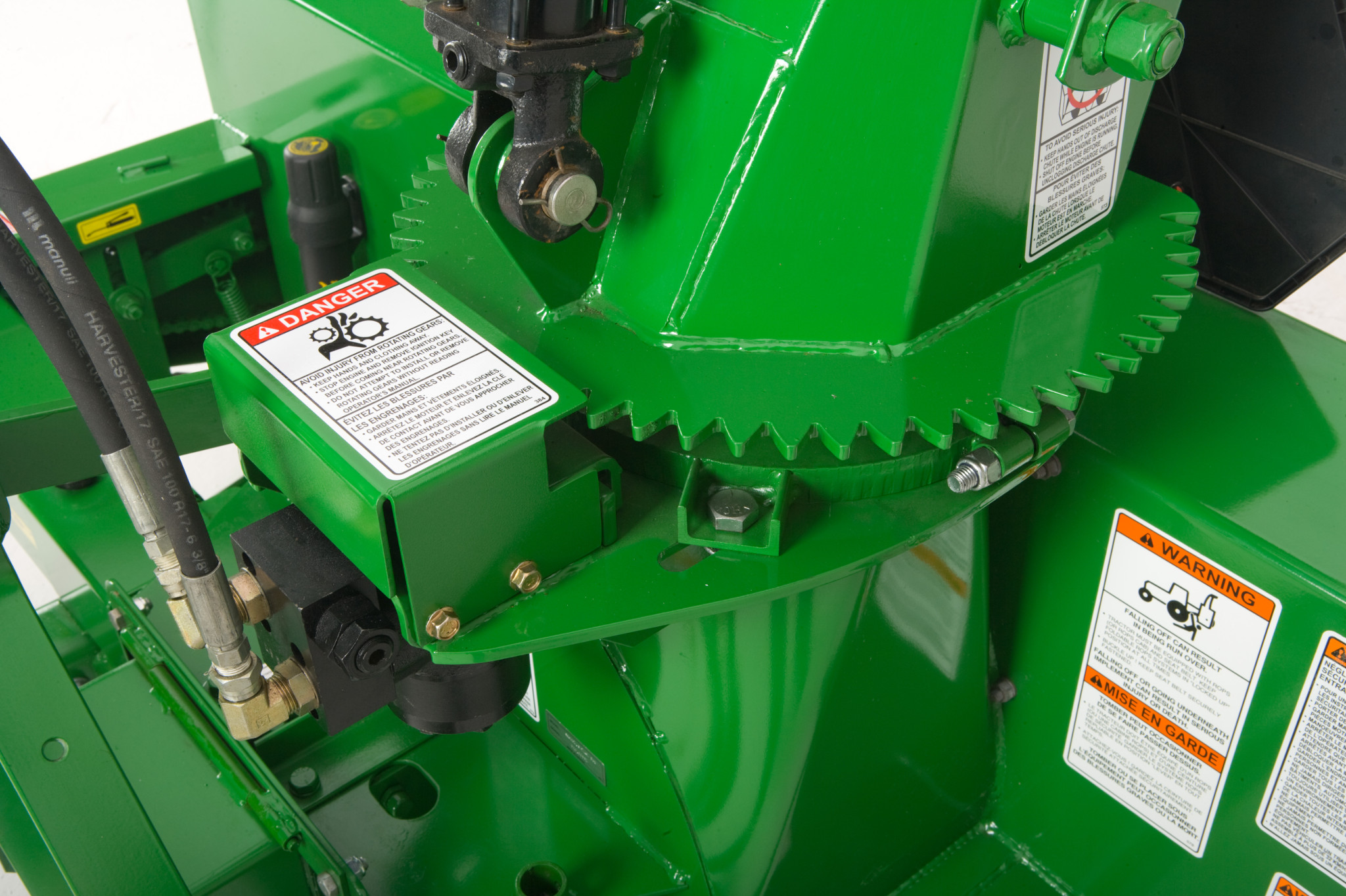 Close-up of snowblower showing a large toothed gear ring and nearby hydraulic components with visible safety labels