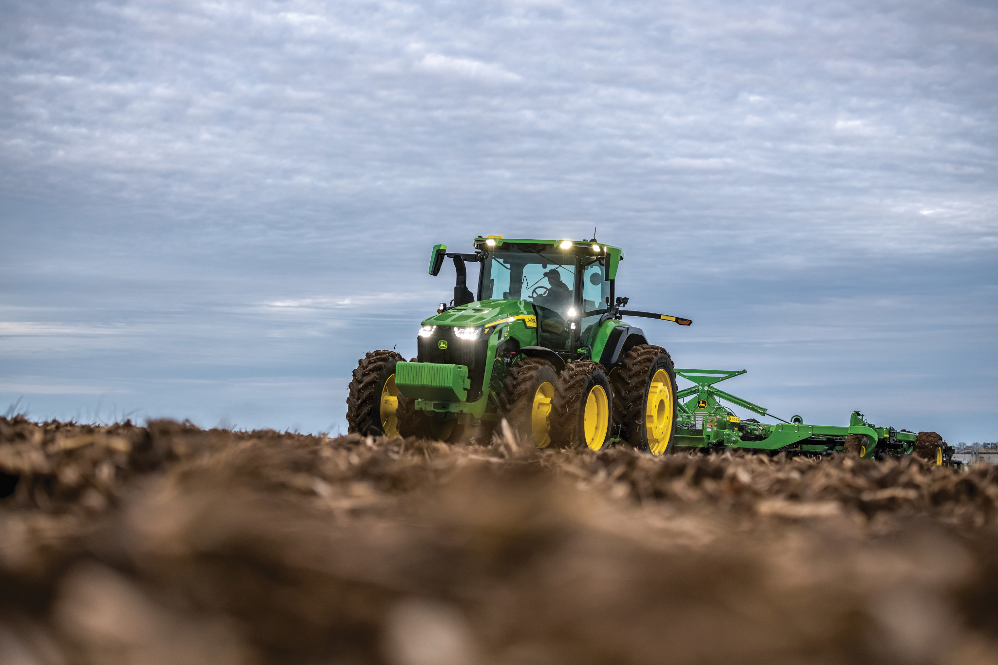 John Deere 8R tractor tilling a field at dusk — Koenig Equipment