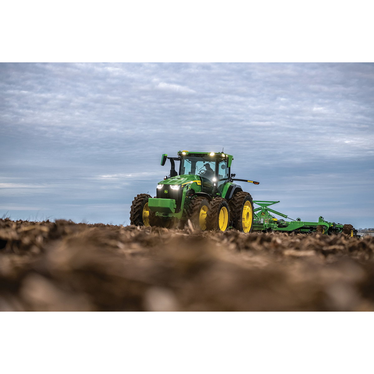 John Deere 8R tractor tilling a field at dusk — Koenig Equipment
