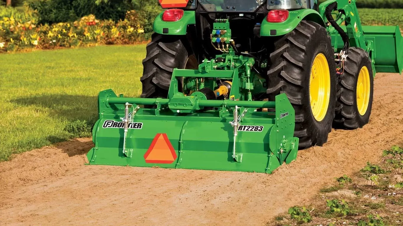Frontier RT22 series rotary tiller on the back of a tractor on a dirt road