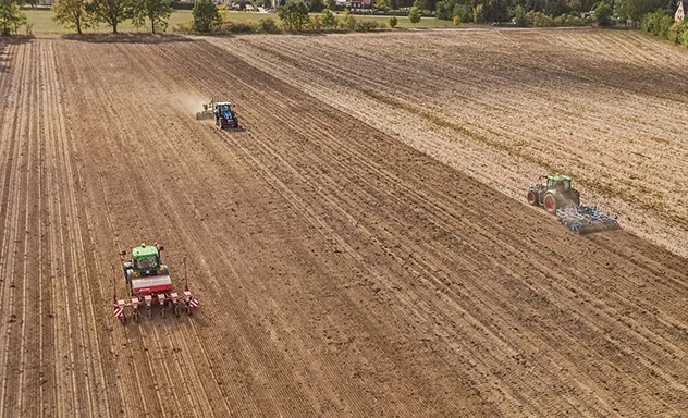 Overhead view of three tractors pulling implements along parallel rows in a field