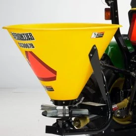 Close up, front left studio view of a yellow SS3067B broadcast spreader with orange high-vis triangle pasted to the side. Part of the attached tractor is visible.
