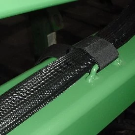 Close-up of a black braided hose secured to a green metal frame with a plastic clamp