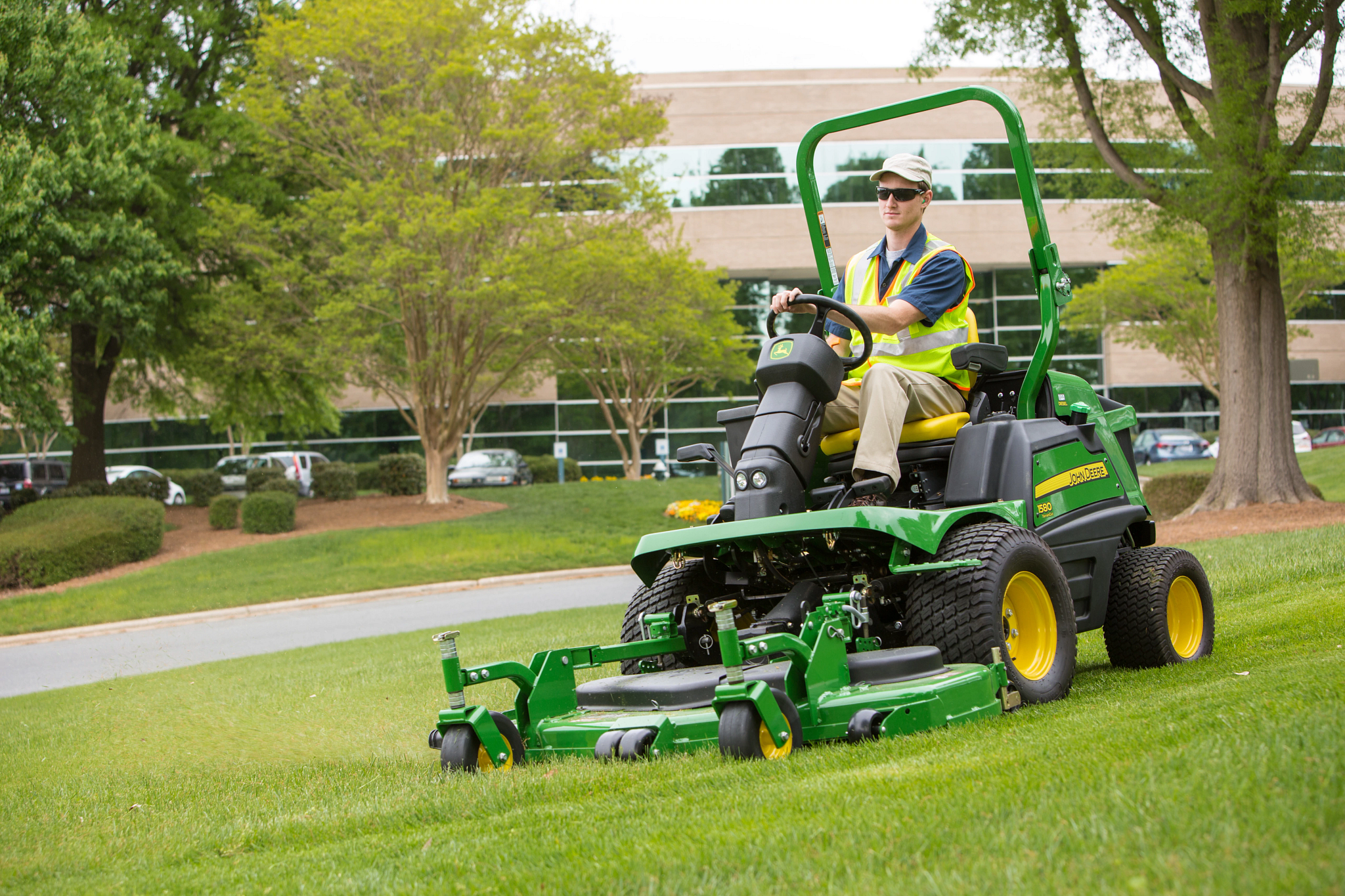 Front left view of a yellow-vested operator on a 1580 TerrainCut™ Front Mower mowing a lawn in front of a business