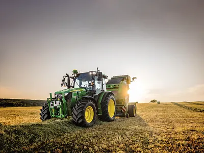 Vue avant gauche d’un tracteur de la série 5M tirant une presse à balles dans un champ