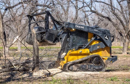 Side left view of a MK76 Mulching Head on a 335 P-Tier compact track loader mulching a standing tree trunk in a park