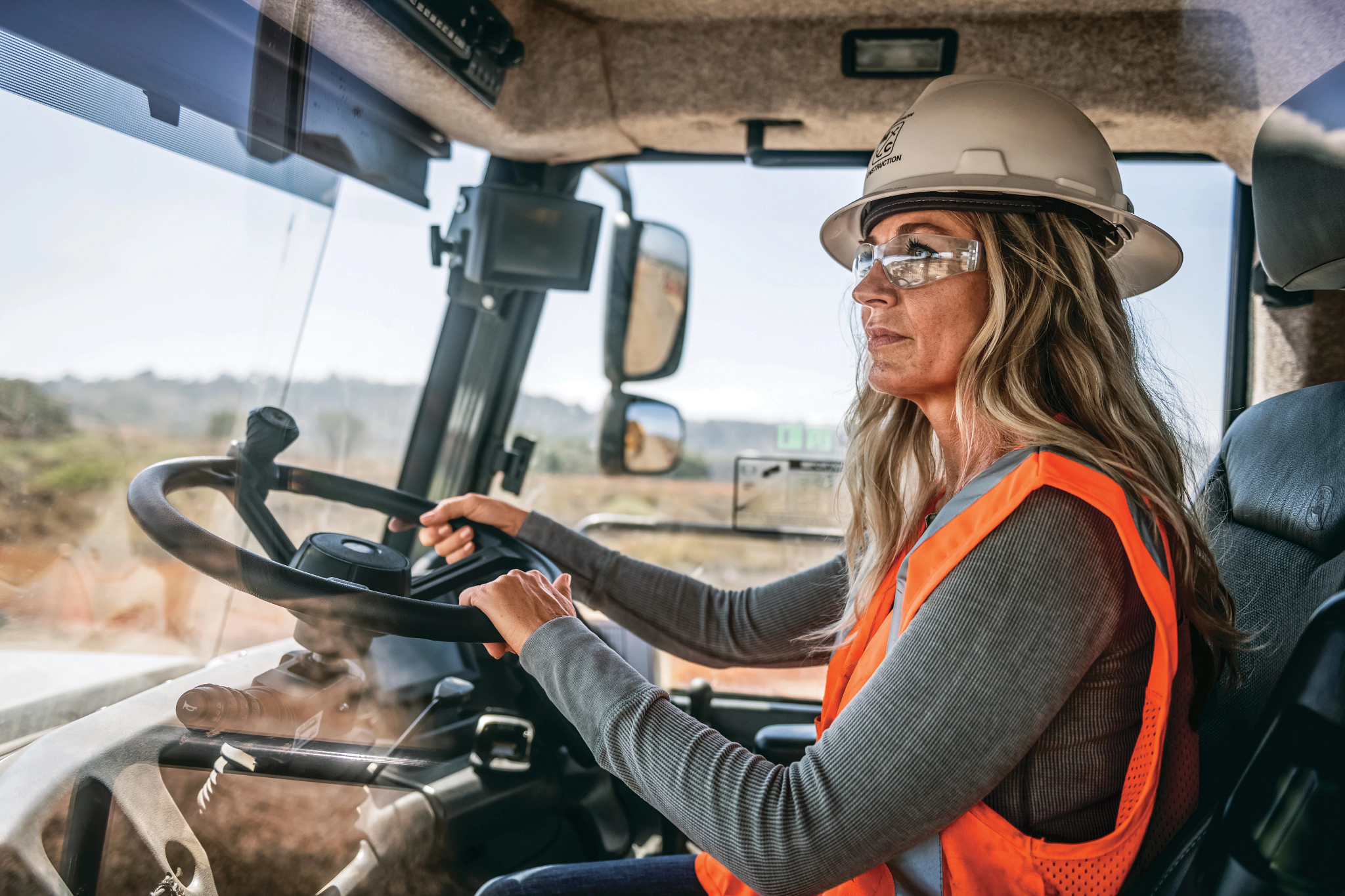 Operator in orange vest inside dump truck cab