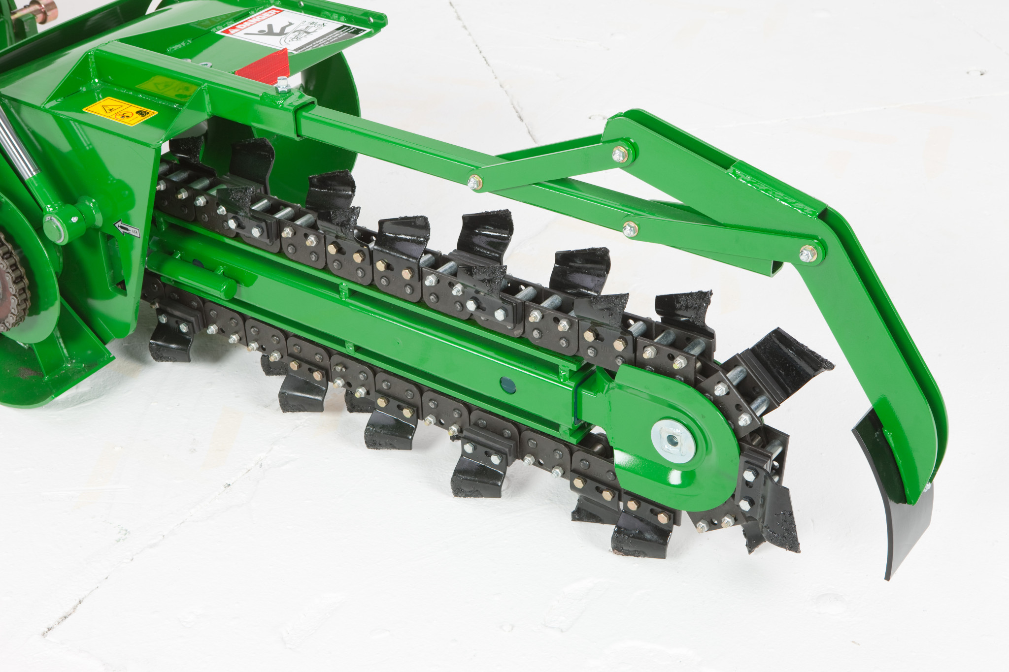 Close-up view of a green trenching attachment with a rotating chain of digging teeth and a curved skid shoe, shown on a white background