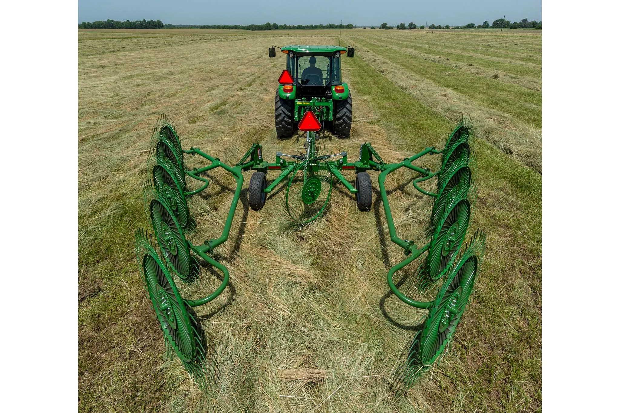 Rear view of a tractor pulling a WR00 wheel rake across a hay field