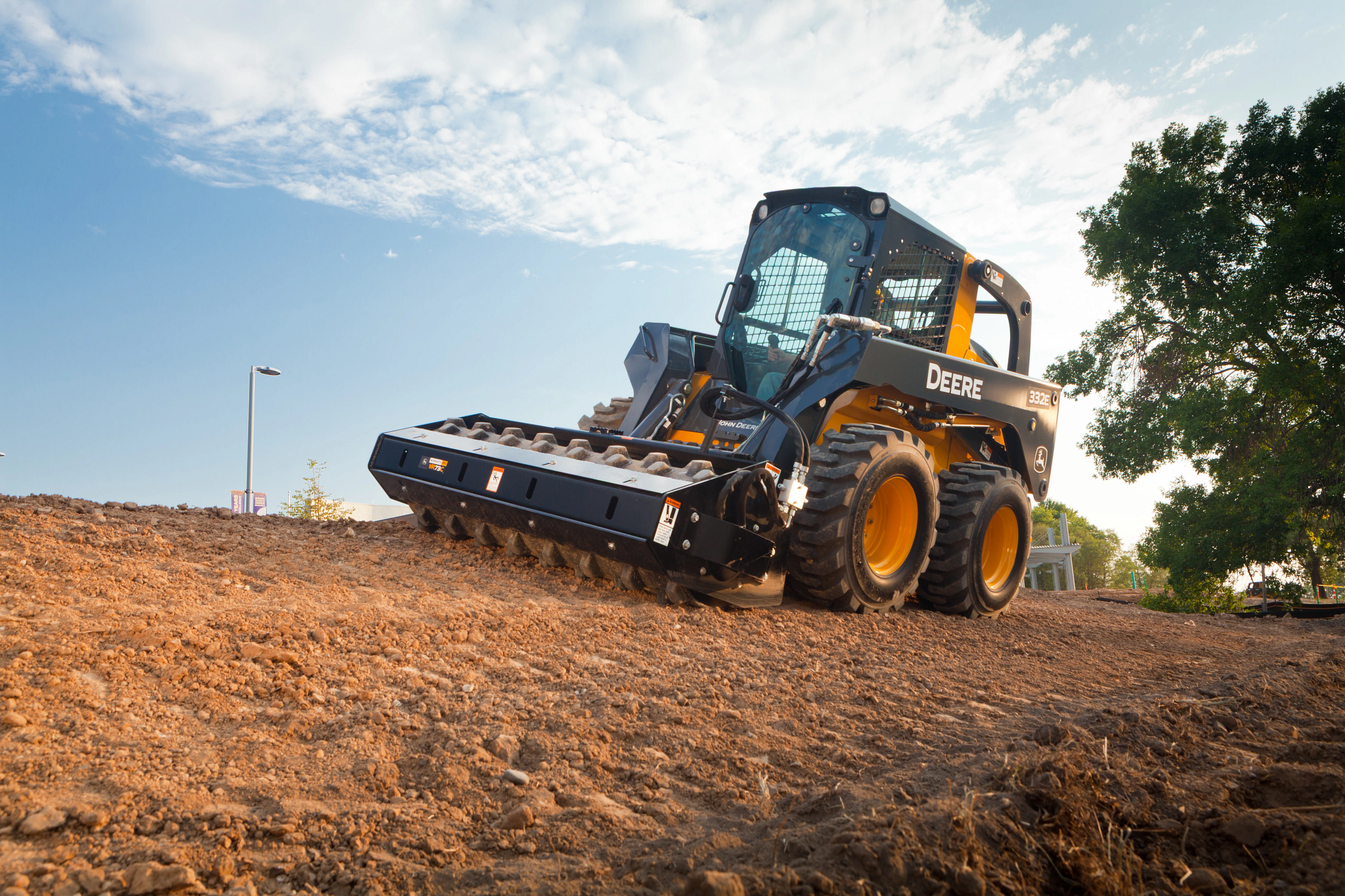 Skid steer loader with a front grading attachment working on a dirt slope.