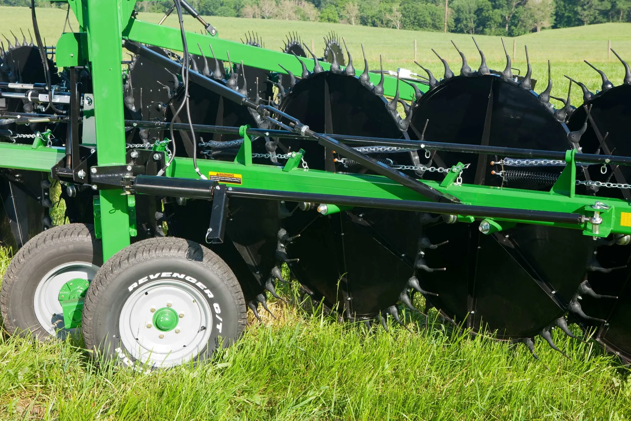 Side close-up of a WR High-Capacity Wheel Rake's black circular components, frame, and wheels parked in grass