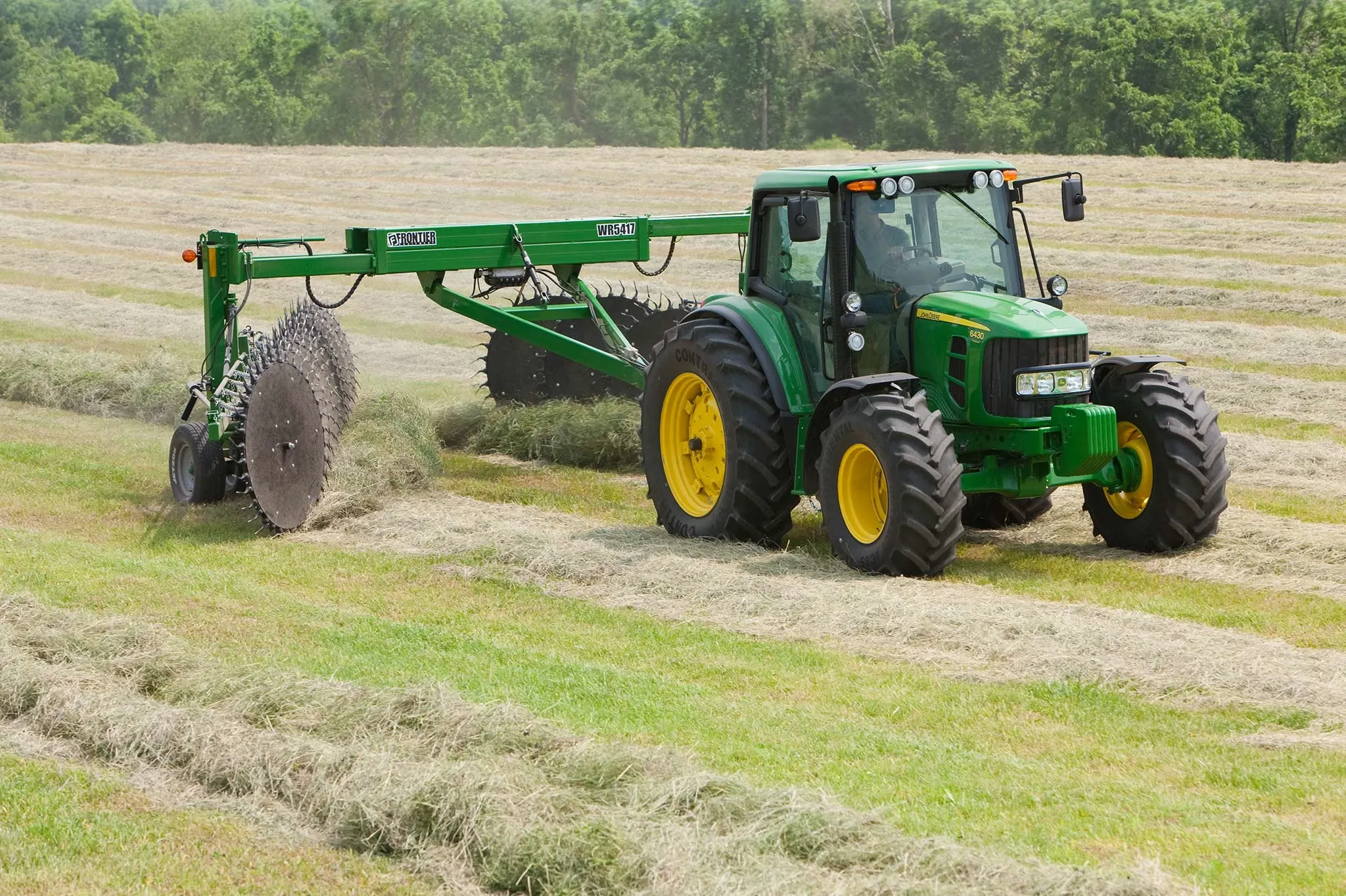 Front right view of a tractor and WR5417 wheel rake at work on windrows in a tree-lined hay field