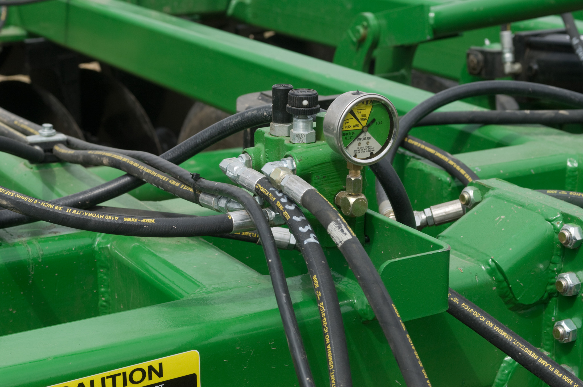 Close-up of tandem disk harrow with multiple hydraulic hoses connected to fittings and a pressure gauge mounted on the frame