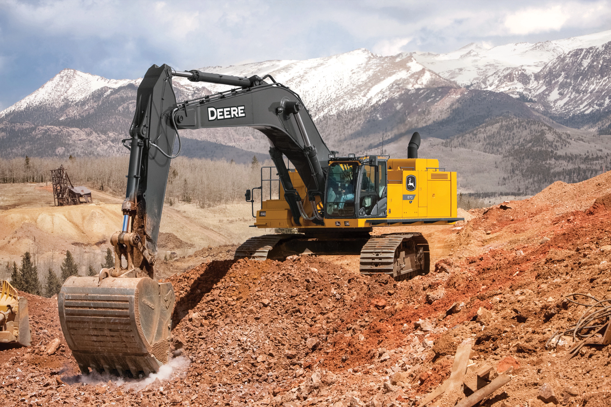 Yellow John Deere tracked excavator positioned on a rocky dirt slope, using a large metal bucket to scrape or move soil