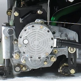 Close-up of a mechanical reel motor assembly with a circular metal component featuring vent-like patterns, surrounded by bolts and connected linkages