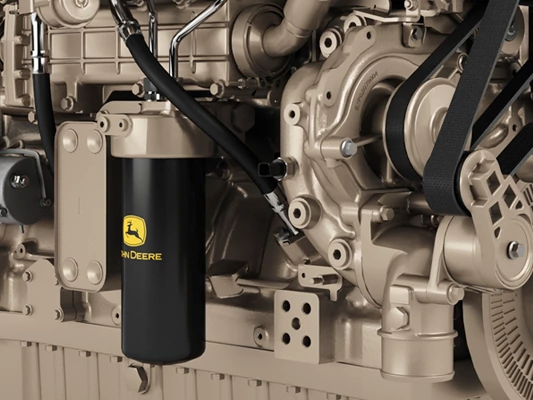 Close-up view of an industrial engine with a black John Deere oil filter, belt-driven pulley system, and metallic engine housing