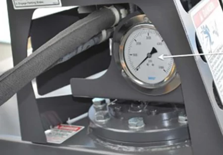 Close-up view of a gray pressure gauge nestled with cables inside a metal protective cage.