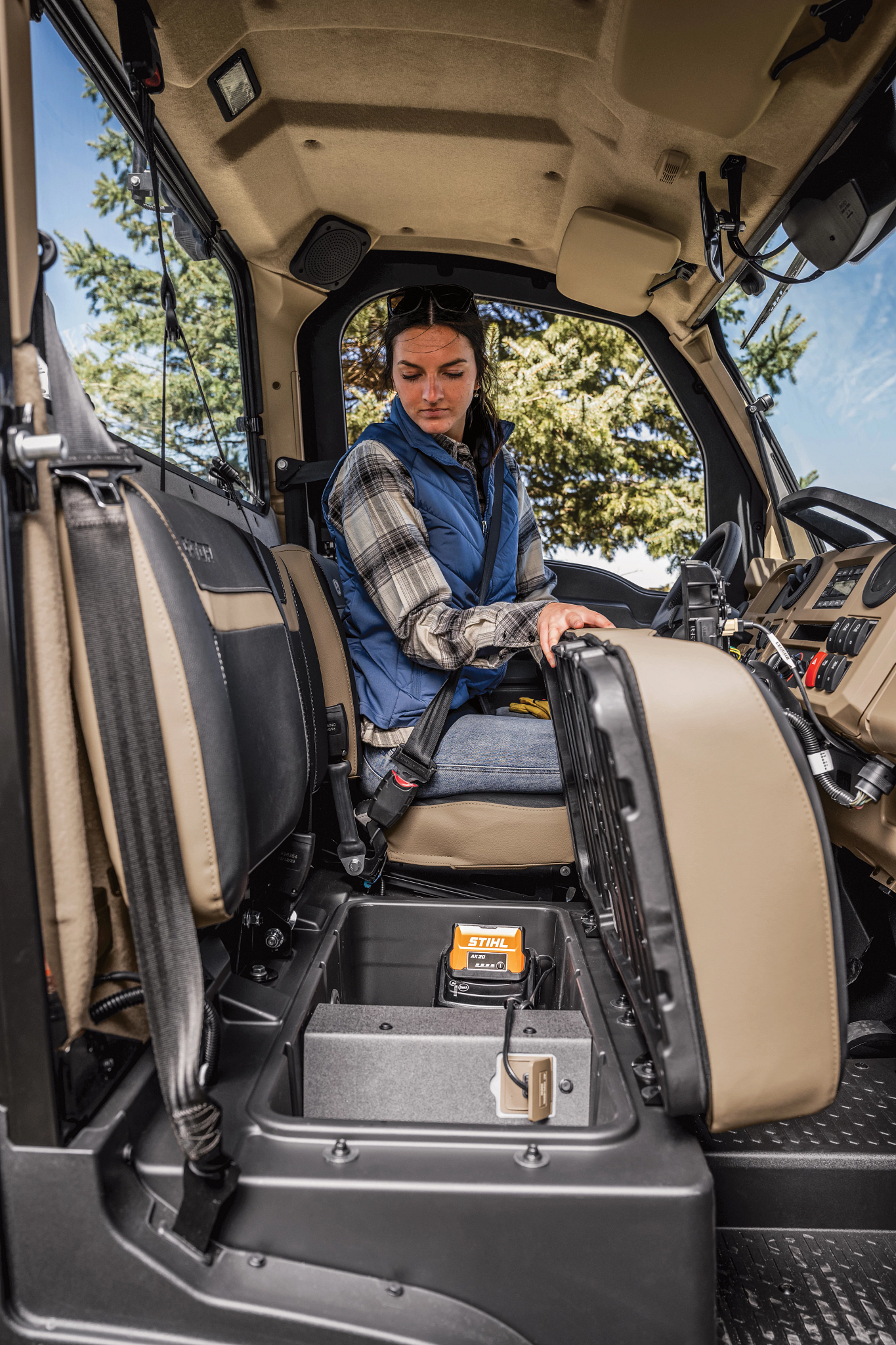 View of an XUV845R Gator's interior from the passenger-side door, with operator holding the bench up and peering at the storage below