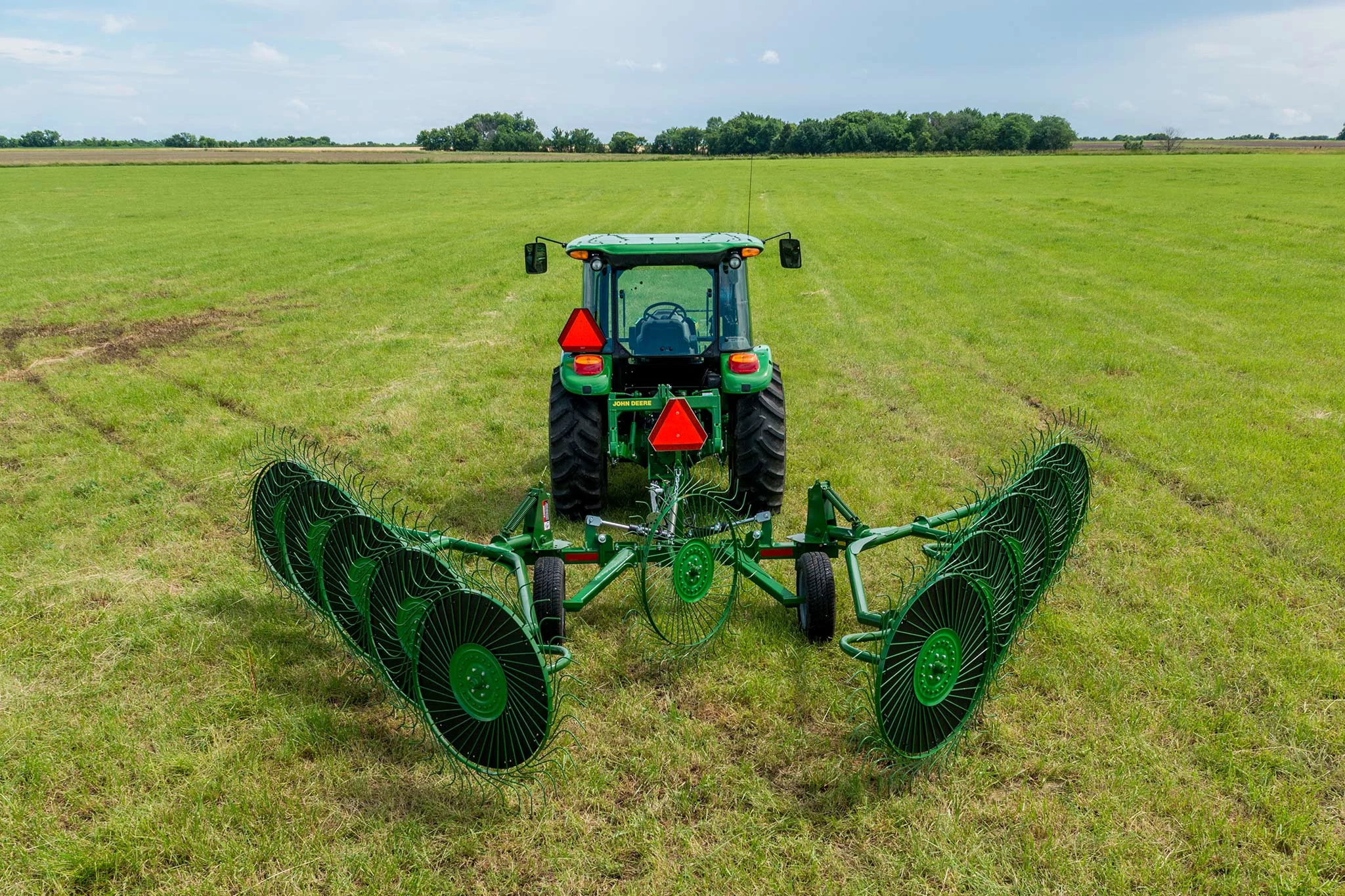 Rear view of a tractor in a grass field with rear-attached WR00 series wheel rake