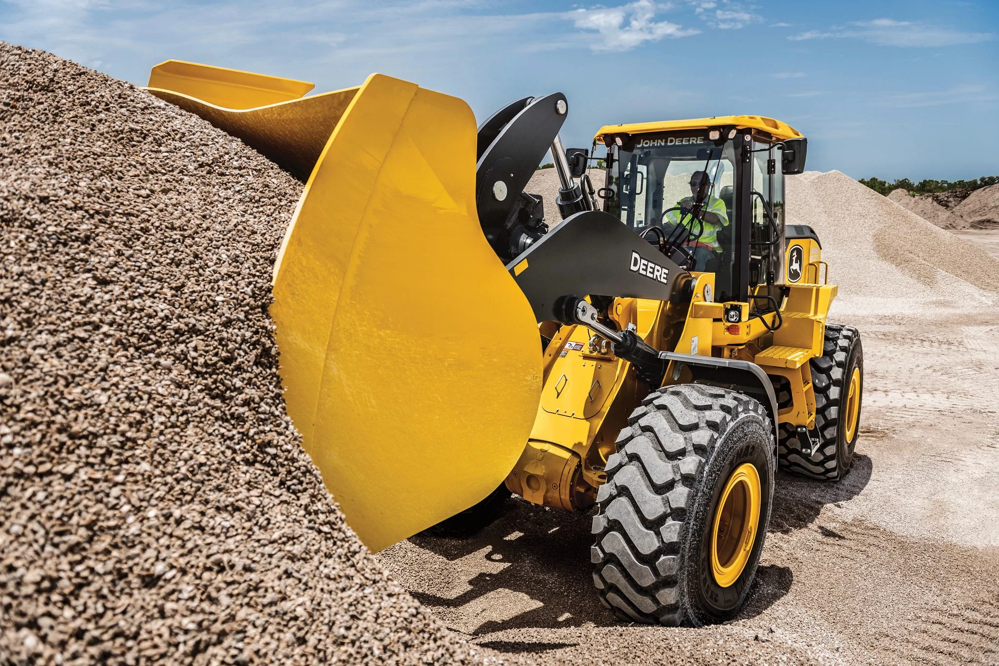 644 G-Tier wheel loader lifting a wide bucket into a large pile of gravel at a construction site.
